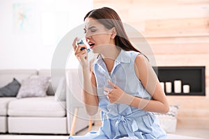 Young woman with asthma inhaler in room