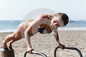 Young woman athlete doing push-ups on parallel bars during her workout at a beach gym