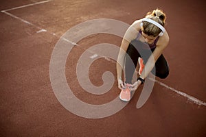 Young  woman athlete with  earphones listening to music and tying laces during training in park with sunset and sunbeam on