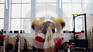 Young woman athlete performs a long cycle push with kettlebell. Girl in gym doing fitness and sports exercises with