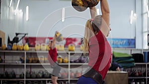 Young woman athlete performs a long cycle push with kettlebell. Girl in gym doing fitness and sports exercises with