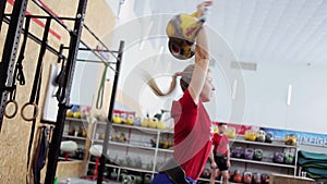 Young woman athlete performs a long cycle push with kettlebell. Girl in gym doing fitness and sports exercises with