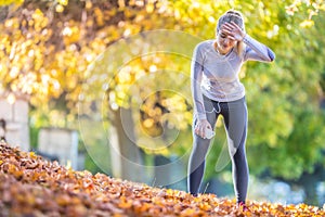 Young woman athlete runner tired breathing after running in a beautiful colorful autumn park