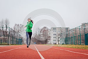 Young woman athlete running on sportsground in autumn. Full body portrait. Active healthy lifestyle