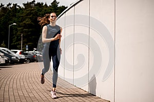 Young woman athlete running on urban city street in front of white wall in morning