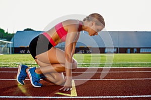 Young woman athlete at starting position ready to start a race on racetrack.