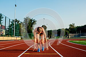 Young woman athlete at starting position ready to start a race on racetrack.