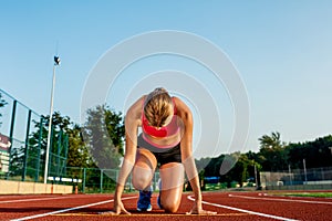 Young woman athlete at starting position ready to start a race on racetrack.