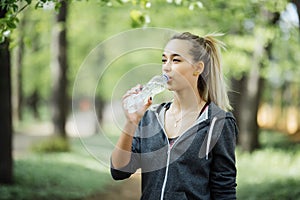 Young woman athlete takes a break, she drinking water, out on a run on a hot day