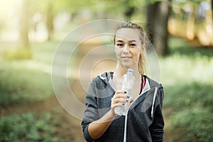 Young woman athlete takes a break, she drinking water, out on a run on a hot day