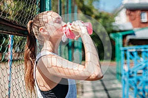 Young woman athlete takes break, she drinking water, out on a run on hot day