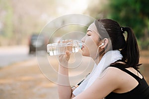 Young woman athlete takes a break, drinking water, out on a run on a hot day.