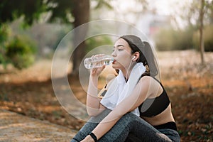 Young woman athlete takes a break, drinking water, out on a run on a hot day.