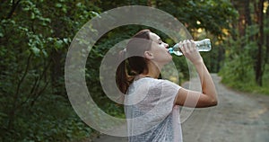 Young woman athlete takes a break, drinking water, out on a run on a hot day.