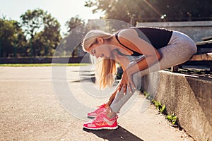 Young woman athlete touching her ankle after running on sportsground in summer. Injury during training