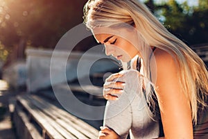 Young woman athlete touching her knee after running on sportsground in summer. Injury during training