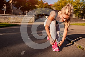 Young woman athlete tying sneakers on running track on sportsground in summer. Preparation for training