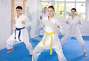Young woman attendee of karate classes practicing kata standing in row with others