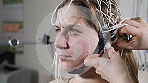 Young woman attending clinic for neurological evaluation using EEG machine. Female doctor operating
