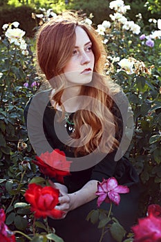 Young woman with auburn hair sitting in the rose garden