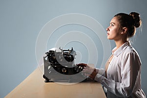 young woman author at a typewriter, writes a text. A writer at a table with a vintage typewriter