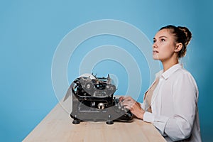 young woman author at a typewriter, writes a text. A writer at a table with a vintage typewriter