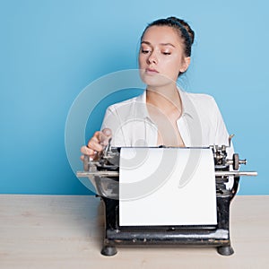 young woman author at a typewriter, writes a text. A writer at a table with a vintage typewriter