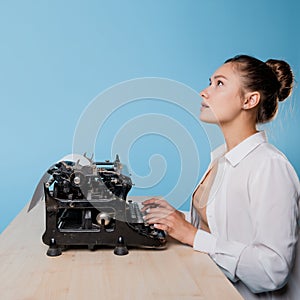 young woman author at a typewriter, writes a text. A writer at a table with a vintage typewriter