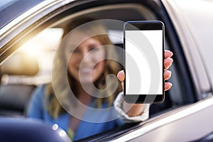 Young woman in auto shows smartphone with blank screen.