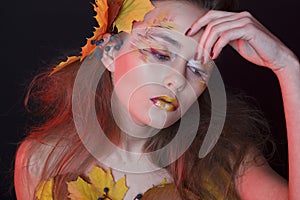 Young woman with autumn make up and leaves on head and her body