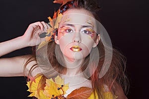 Young woman with autumn make up and leaves on head and her body