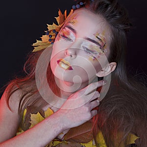 Young woman with autumn make up and leaves on head and her body