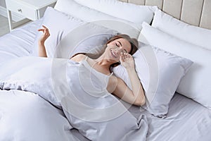 Young woman awaking in bed with silky linens