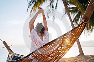 Young woman awaking and meeting morning sunrise sunlight sitting in a hammock and lazy stretching her body raising arms up on the photo