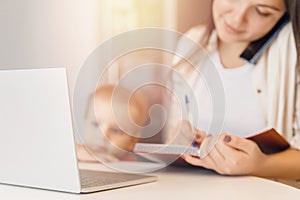 Young woman with baby speaks by phone and working with laptop on kitchen. Business Quarantine Concept