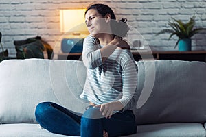 Young woman with back pain sitting on the sofa in the living room at home