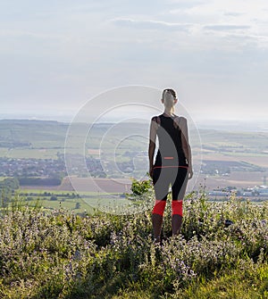 Young woman from back standing on lookout in fitness outfit looking to valley. Palava, Czech republic