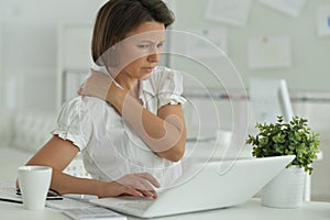 Young woman with backache using laptop in office