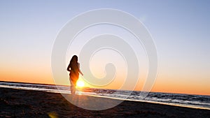 A young woman on the background of the sunset the sun on the seashore does exercises exercised by running, stretching and slumping