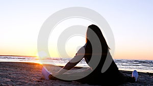 A young woman on the background of the sunset the sun on the seashore does exercises exercised by running, stretching and slumping