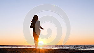 A young woman on the background of the sunset the sun on the seashore does exercises exercised by running, stretching and slumping