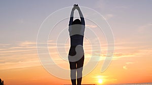 A young woman on the background of the sunset the sun on the seashore does exercises exercised by running, stretching and slumping