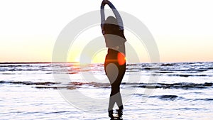 A young woman on the background of the sunset the sun on the seashore does exercises exercised by running, stretching and slumping