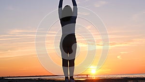 A young woman on the background of the sunset the sun on the seashore does exercises exercised by running, stretching and slumping