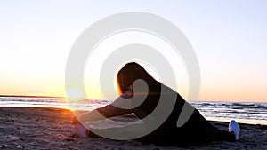 A young woman on the background of the sunset the sun on the seashore does exercises exercised by running, stretching and slumping