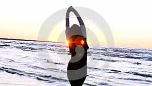A young woman on the background of the sunset the sun on the seashore does exercises exercised by running, stretching and slumping