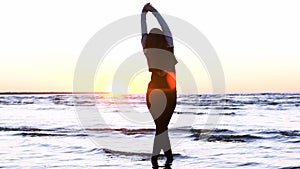 A young woman on the background of the sunset the sun on the seashore does exercises exercised by running, stretching and slumping