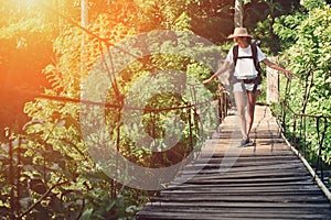 Young woman with backpack and hat traveling over hanging bridge