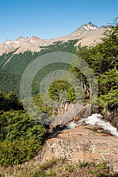 A young woman with backpack hiking and sitting on rocks and snow and enjoying the views of the Andes mountains and lake hiking Vil photo