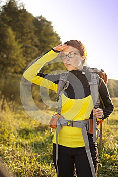 Young woman with backpack in a meadow watches way . Hiking at summertime.